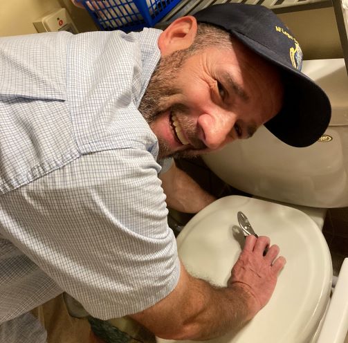 Tim fixing a toilet and smiling at the camera